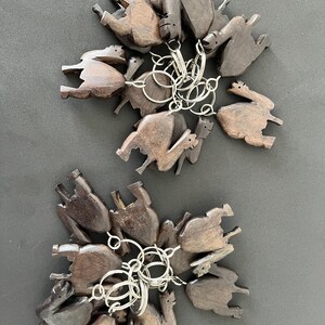 Op de afbeelding: Een set van 12 houten kameel sleutelhangers, elk met een donkerbruine afwerking. De sleutelhangers zijn gerangschikt in twee groepen, met een zilveren sleutelring die elke groep verbindt.