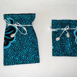 May include: Two fabric pouches with a blue and black polka dot pattern. The pouches are tied with white string and have white seashells as accents.