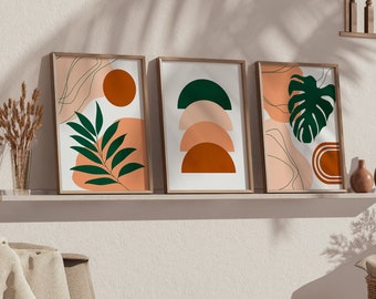 May include: Three abstract art prints featuring geometric shapes and foliage in shades of green, orange, and brown. The prints are framed and hung on a white wall above a shelf with decorative items.