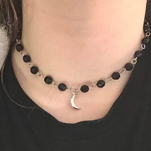 May include: A black beaded choker necklace with a silver crescent moon pendant.