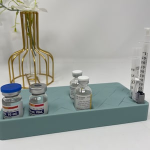 Puede incluir: Una bandeja de silicona azul claro con cuatro peque&ntilde;os viales de vidrio y una jeringa. Los viales est&aacute;n etiquetados con "10 mL VIAL" y "0,9% Cloruro de Sodio".