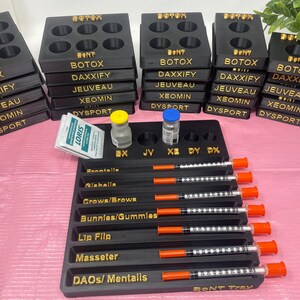 May include: A black plastic tray with eight compartments labeled with different types of Botox and fillers. The tray is filled with syringes and vials of medication. The tray is labeled "BONT TRAY".