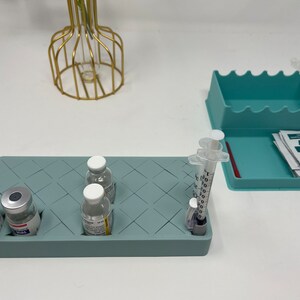 Puede incluir: Una bandeja de silicona azul claro con un patr&oacute;n de diamante contiene cuatro viales de vidrio transparentes y una jeringa. La bandeja est&aacute; sobre una superficie blanca. La jeringa est&aacute; etiquetada con 100, 80, 60, 40, 20 y 10.