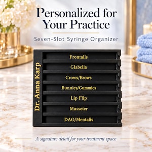 May include: A black seven-slot syringe organizer featuring gold text labels for Frontalis, Glabella, Crows/Brows, Bunnies/Gummies, Lip Flip, Masseter, and DAO/Mentalis, with the name Dr. Anna Karp printed vertically on the left side.