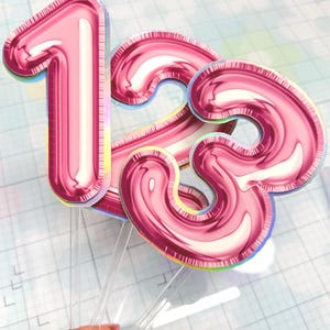 Könnte beinhalten: Rosafarbene Tortenaufsatz mit der Zahl 13 in Ballonoptik. Die Zahlen sind an transparenten Kunststoffstäben befestigt, um sie einfach in einen Kuchen stecken zu können. Der Aufsatz hat einen holografischen Effekt.