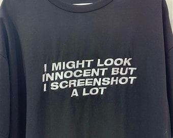 May include: Black t-shirt with white text that reads "I might look innocent but I screenshot a lot".