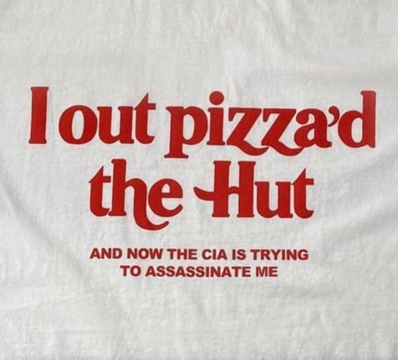 Pode incluir: Camiseta branca com texto vermelho que diz "I out pizza'd the Hut" e "And now the CIA is trying to assassinate me."