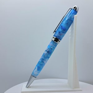Op de afbeelding: Een blauwe en witte pen met een swirl-patroon, met een zilveren clip en dop. De pen staat op een witte standaard.