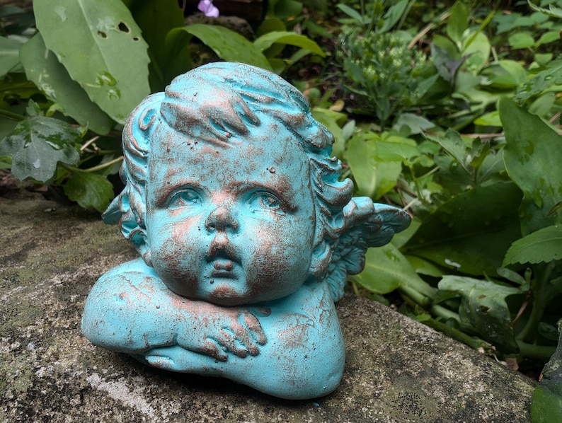 May include: A turquoise blue cherub statue with wings, a cherubic face, and a distressed finish.