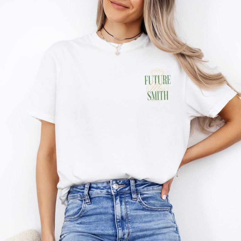 Pu&ograve; includere: Maglietta bianca con una grafica verde e oro di un anello di diamanti e il testo "Future Mrs. Smith"