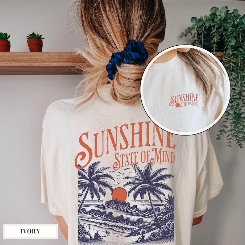 May include: Ivory t-shirt with a graphic print of palm trees, waves, and a sunset. The text "Sunshine State of Mind" is printed in orange on the back of the shirt.