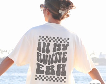 May include: Ivory t-shirt with a black and white checkered border and the text "In My Auntie Era" in a retro font.