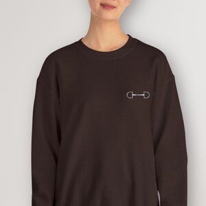 May include: A dark brown sweatshirt with a white equestrian bit design on the front.