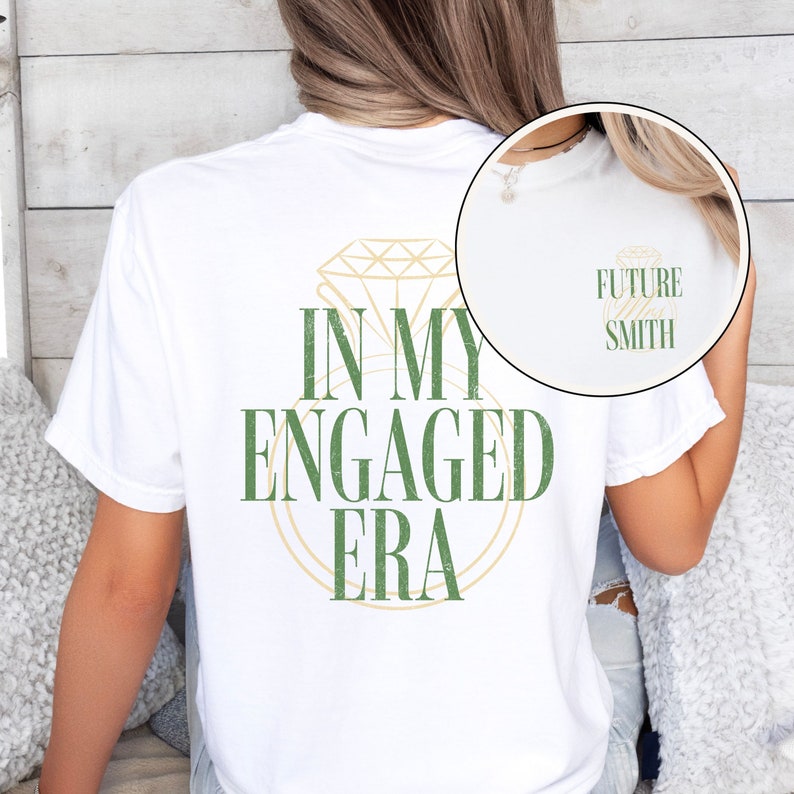 Pu&ograve; includere: Maglietta bianca con una grafica verde di un anello di diamanti e il testo "In My Engaged Era". La parte posteriore della maglietta ha il testo "Future Smith" in un carattere pi&ugrave; piccolo.