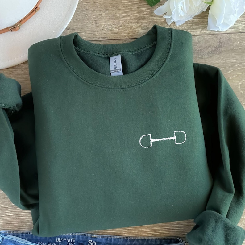 May include: A dark green sweatshirt with a white embroidered equestrian bit design.