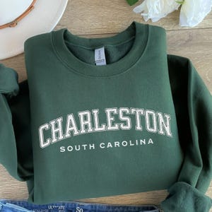 May include: A dark green sweatshirt with white text that reads "CHARLESTON SOUTH CAROLINA".