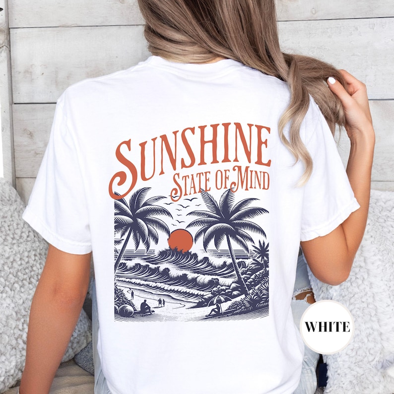 May include: White t-shirt with a graphic of palm trees, waves, and a sunset. The text "Sunshine State of Mind" is printed above the graphic.