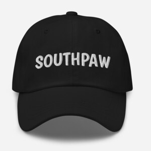 Pode incluir: Um boné de beisebol preto com texto bordado em branco que diz "SOUTHPAW".