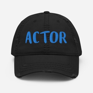 Peut inclure: Casquette de baseball noire usée avec le mot "ACTOR" brodé en bleu.