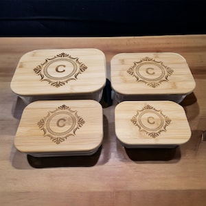 May include: Four square glass containers with bamboo lids. Each lid has a decorative design with the letter "C" in the center.