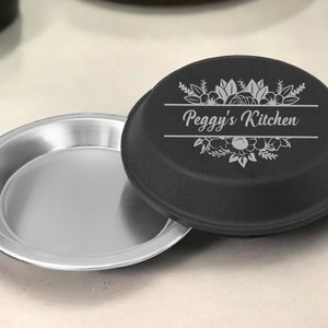 May include: Black pie pan with a silver lid. The lid has a floral design and the text "Peggy's Kitchen" engraved on it.