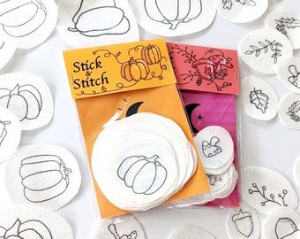 May include: A set of white felt patches with various fall-themed designs, including pumpkins, acorns, leaves, and mushrooms. The patches are packaged in two clear plastic bags with orange and pink labels that say "Stick & Stitch".