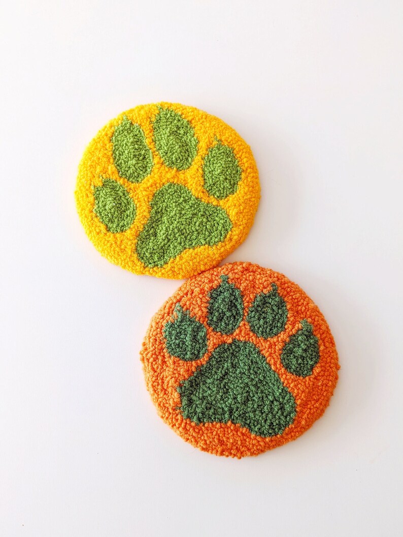 May include: Two round, plush, orange and green paw print coasters. The paw prints are green and the background is orange.