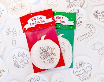 May include: A set of white, round, Christmas-themed stickers with black outlines. The stickers feature images of a gingerbread house, a candy cane, a stocking, a mitten, a cupcake, a holly sprig, and a gingerbread man. The stickers are packaged in two clear plastic bags with red and green labels that say "Fa La La La La La" and "Ho! Ho! Ho!"