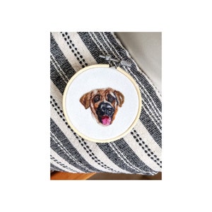 Puede incluir: La cara de un perro marr&oacute;n y beige est&aacute; bordada en una tela blanca estirada sobre un aro de bordado de madera.