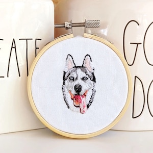 Puede incluir: Retrato bordado de un perro husky con ojos azules y la lengua rosa que sobresale, enmarcado en un aro de madera redondo.