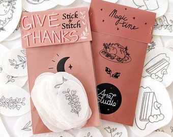 May include: Two rectangular packaging cards in dusty rose with black line art designs. The left card reads GIVE THANKS Stick & Stitch, and the right card reads Magic time with Aria Studio logo. Both contain white adhesive embroidery patterns.