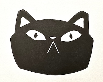 May include: A black cat face illustration with white eyes, nose, and ears on a white background. The cat's face is a simple geometric design. The text "August Midnight" is written in cursive at the bottom.