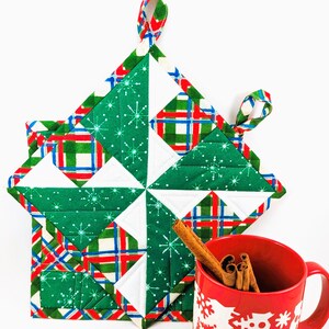 May include: Two green, red and white quilted pot holders with snowflake patterns and a red mug with white snowflake designs and cinnamon sticks inside.