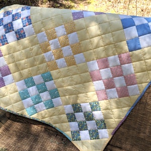 Puede incluir: Una colcha amarilla con un diseño de patchwork que presenta cuadrados de diferentes colores y patrones, incluyendo morado, azul, rosa, verde y amarillo. La colcha está hecha con una variedad de telas y está acolchada con una puntada simple.