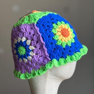 May include: A colorful crocheted bucket hat with a green brim and a patchwork design of purple, blue, green, yellow, and orange squares.