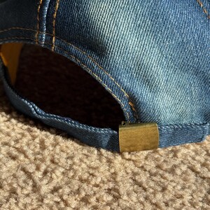 May include: A blue denim baseball cap with a yellow stitch detail and a gold metal buckle closure.