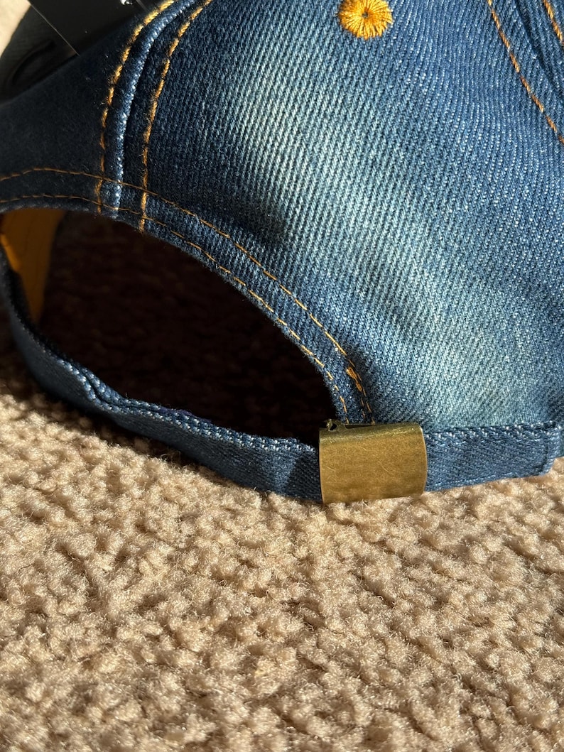 May include: A blue denim baseball cap with a yellow stitch detail and a gold metal buckle closure.