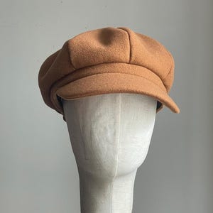 May include: A brown wool newsboy cap with a slightly rounded crown and a wide brim.