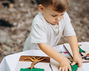 Op de afbeelding: Een jong kind speelt met een houten puzzel met een boom met groene bladeren en een bruine stam. De puzzelstukken zijn los en het kind plaatst ze in de juiste vakjes.
