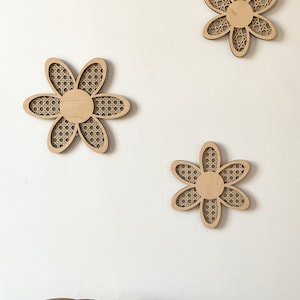 May include: Three wooden wall decor pieces in the shape of a flower with a woven pattern. The flowers are light brown and have a white background.