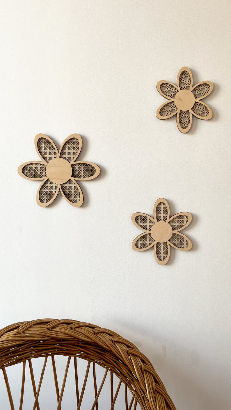 May include: Three wooden wall decor pieces in the shape of a flower with a woven pattern. The flowers are light brown and have a white background.