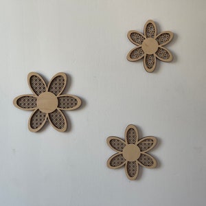 May include: Three wooden wall decor pieces in the shape of a flower with a woven pattern. The flowers are light brown and have a simple design.