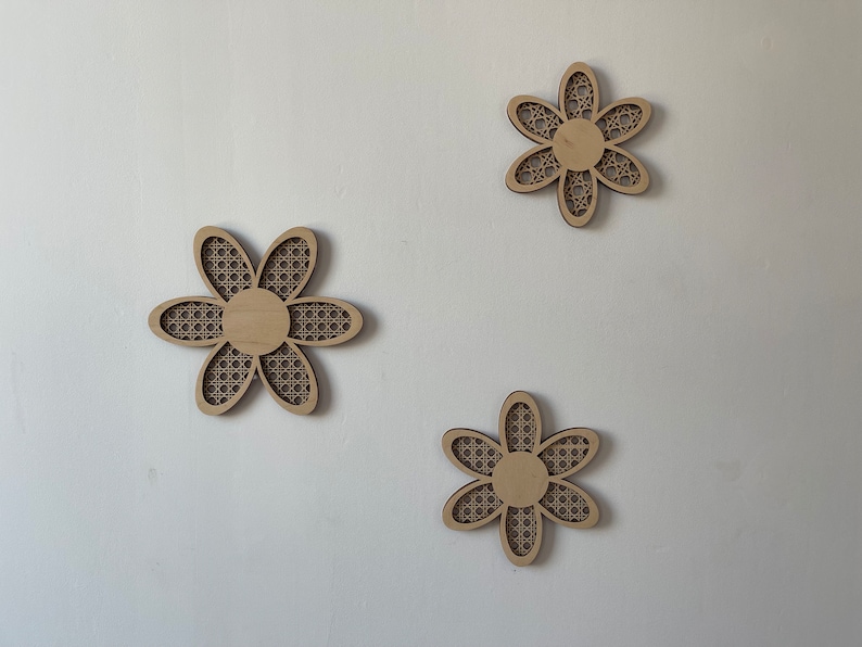 May include: Three wooden wall decor pieces in the shape of a flower with a woven pattern. The flowers are light brown and have a simple design.