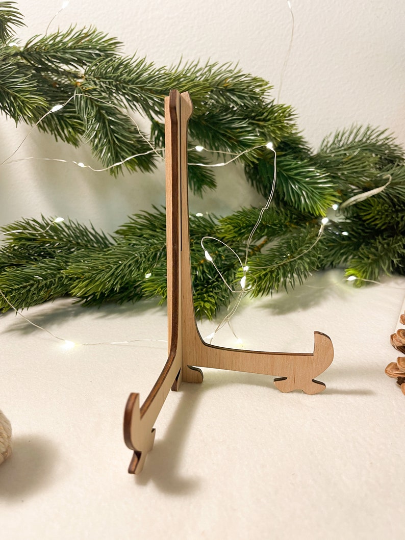 May include: A wooden display stand with a triangular base and three legs. The stand is made of light brown wood and has a natural finish.