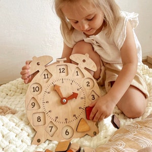 May include: A wooden clock with a movable hand and a removable number and shape puzzle. The clock face has numbers 1 through 12 and markings for 5, 10, 15, 20, 25, 30, 35, 40, 45, and 50. The clock is light brown and has a red hand. The puzzle pieces are various shapes and colors.