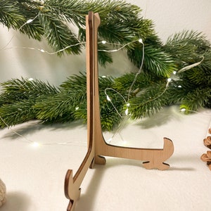 May include: A wooden display stand with a triangular base and three legs. The stand is made of light brown wood and has a natural finish.