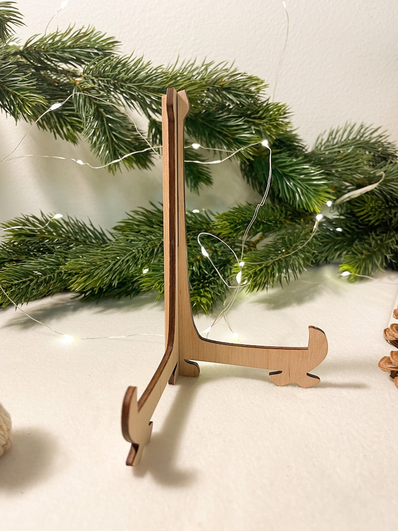 May include: A wooden display stand with a triangular base and three legs. The stand is made of light brown wood and has a natural finish.