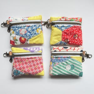 May include: Four small, colorful patchwork zipper pouches. Each pouch features a unique combination of patterned fabrics in red, yellow, blue, and green. They have metal zippers and small leather tabs with a metal clasp.