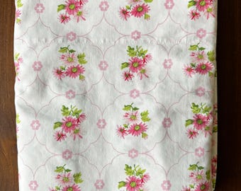 Puede incluir: Sábana blanca doblada con un patrón repetido de flores rosas y hojas verdes. El diseño floral está enmarcado en un patrón de cuadrifolio y cruz rosa claro. La sábana parece ser de algodón.
