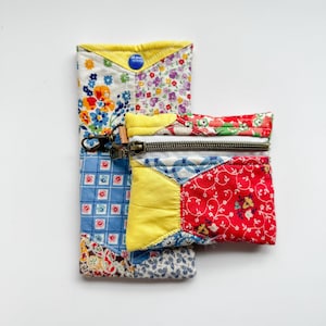 May include: Two patchwork fabric pouches. One is a long, rectangular case with a yellow trim and a blue button closure. The other is a small, square pouch with a zipper closure. Both are made of colorful floral and geometric patterned fabrics.